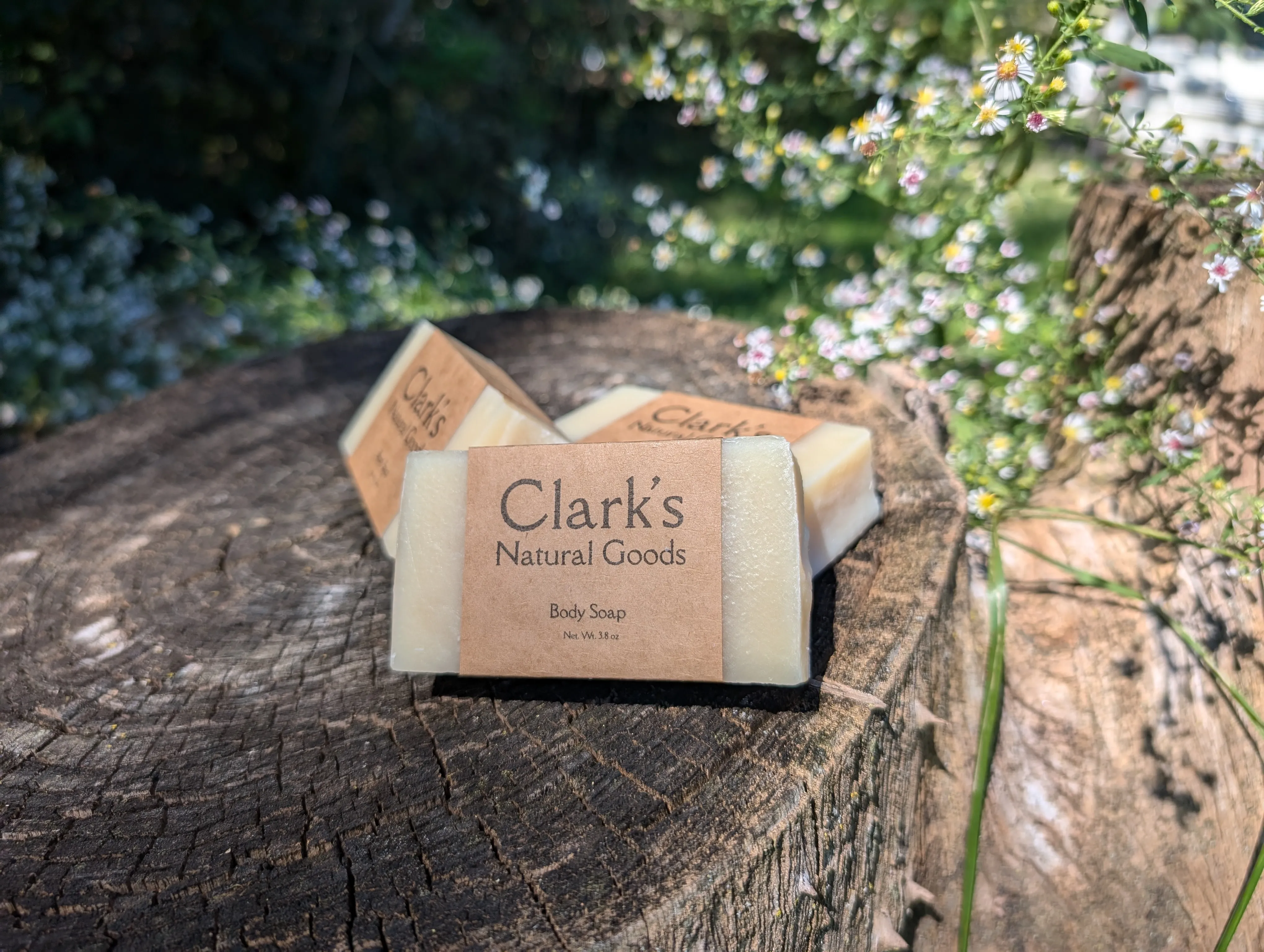 Handmade soap resting on a log surrounded by wildflowers